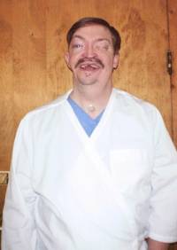 Picture of John Nozum, owner of the company, and wearing a scrub shirt and special lab coat