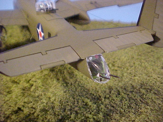 Shot of the modified tail position. The Doolittle Raiders used two wooden broomsticks to simulate machine guns. I had to drill out holes on the solid clear tail cone for the guns, which I made out of stretched sprue so they would look different from the kit machine guns. The white and red formation lights are small blobs of superglue on a piece of styrene strip, glued to the top of the tail compartment. You can also see the different shade of olive drab on the fabric-covered horizontal stabilizers; also note that the trim tab in each is the darker shade because it is metal, not fabric.
