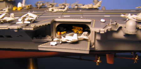 Close-up of the lowered elevator and a Prowler being towed out. Inside, you can see some of the vehicles and a hint of the Hornets lined up against the far wall.