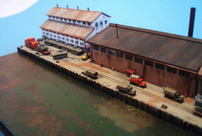 Close-up of the dock area, showing the various trucks, LVTs and tank behind the switching engine.