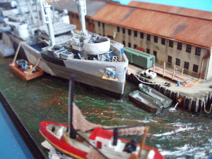 This view shows action on the bow, with some sailors giving one anchor a touch-up paint job, and the paravane hawsers going through an opening in the bow and down to the mine-clearing rig under the bows. The two landing craft tied to the dock are LCP(R)s, also known as the original Higgins boats, which were included in the kit. 